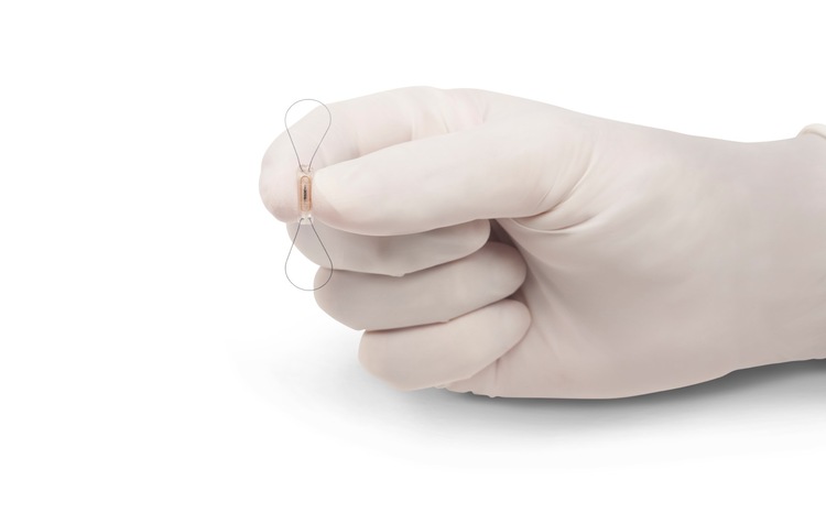 A white gloved hand holding the Abbott CardioMEMS sensor